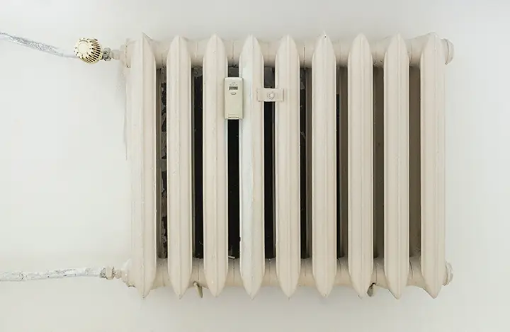 A person in a red shirt and safety glasses inspecting the broken coils of an air conditioner